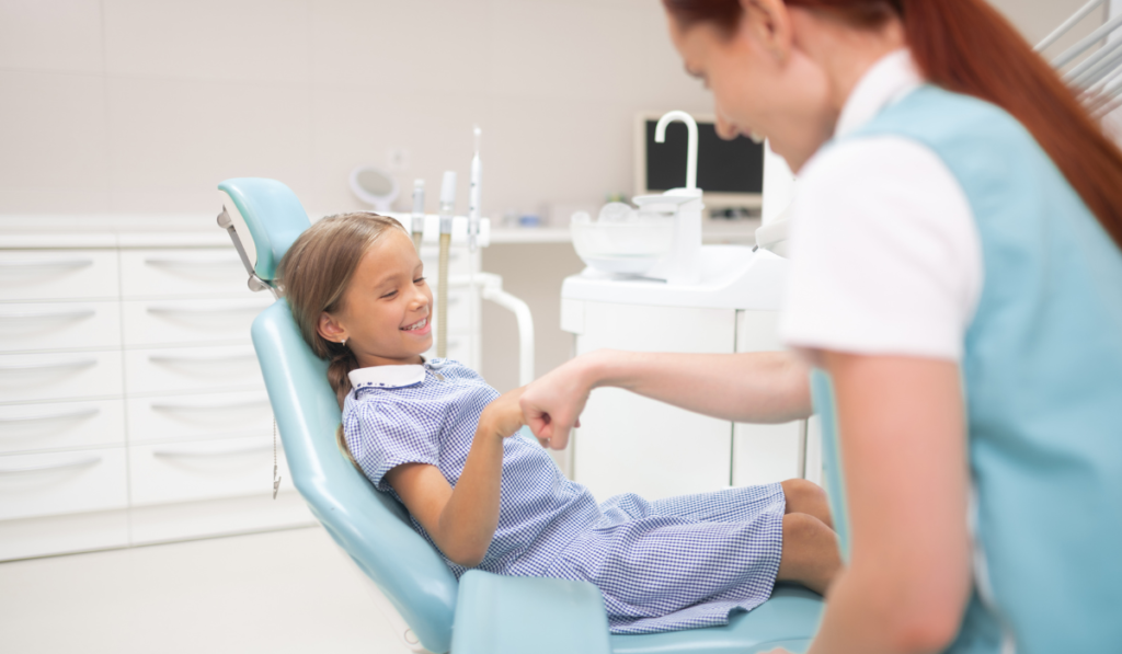 A female representing dental therapists fist-bumping a smiling child in a dentist's chair