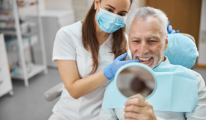 An image of a dental patient holding up a small mirror post-procedure. He's smiling, and the dentist is standing next to him. He may have just received an angled screw channel implant